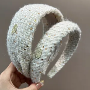 Macro detail of elegant cream tweed padded headband with gold sequins and metal tag
