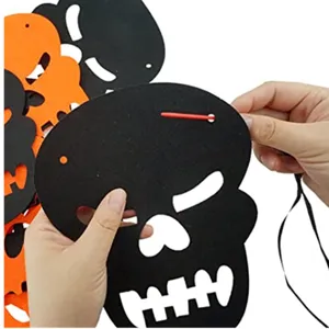 Detail von Händen, die eine schwarze Filz-Totenkopf-Girlande für Halloween fädeln