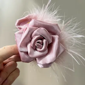 Macro detail of handmade pink satin rose hair clip adorned with soft ostrich feathers