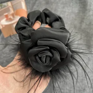 Close-up of elegant black satin scrunchie with handmade camellia and ostrich feathers