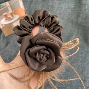 Detailed view of handmade brown satin camellia flower scrunchie with soft ostrich feathers.