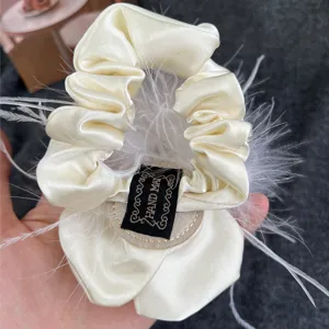 Detailed view of luxury cream satin scrunchie with ostrich feathers and camellia flower