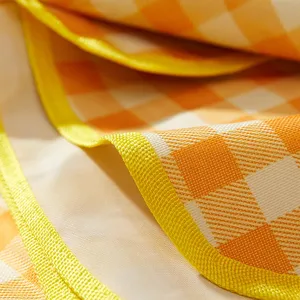 Waterproof picnic mat fabric close up showing detailed yellow checkered texture and edge stitching.