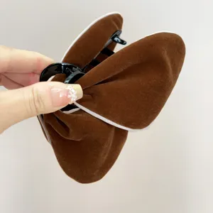 Détail d'une pince à cheveux papillon en velours marron avec liseré blanc décoratif.
