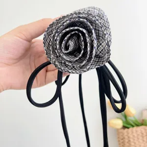 Dettaglio ravvicinato di un fermaglio a rosa 3D a quadri con eleganti nastri neri.