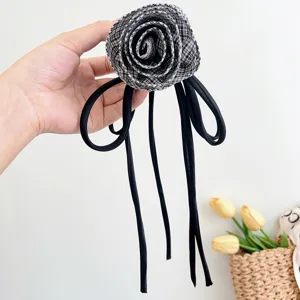 Vista dettagliata di una pinza per capelli con rosa a quadri e lunghi nastri neri.