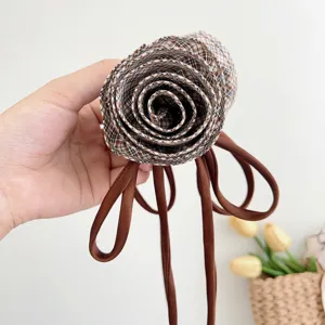 Dettaglio della rosa in tessuto a scacchi marroni e dei lunghi nastri sulla clip per capelli