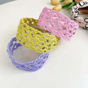 Close-up of three woven straw wide headbands in pink, yellow, and purple holiday colors