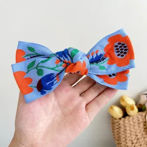 Gros plan d'une pince à cheveux bohème brodée en forme de nœud bleu tenue dans une main.