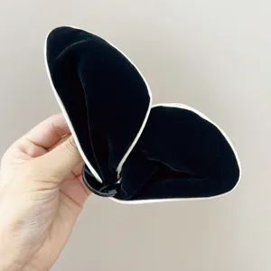 Détail rapproché d'une pince à cheveux papillon en velours noir avec liseré blanc.