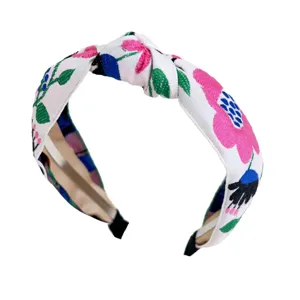 Serre-tête noué brodé de fleurs bohèmes avec une base blanche et des motifs roses.