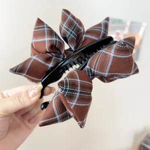 Close-up of a vintage brown plaid bow hair claw clip showing fine tartan fabric texture.