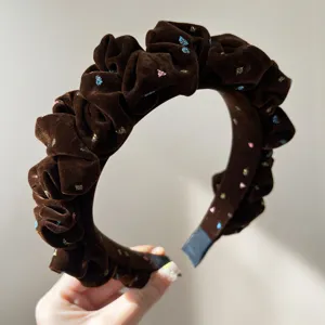 Close-up of a brown velvet ruffled headband with sparkling colorful star patterns