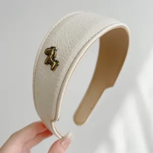 Nahaufnahme eines weißen Vintage-Leder-Haarreifens mit einem kleinen Bronze-Pferd-Detail.