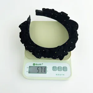 Close-up of a black flocked pleated headband with rhinestones being weighed on a scale