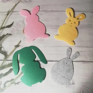 Rabbit-shaped felt cutlery holders in pink, yellow, green, and grey on a wood surface