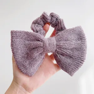 Detailopname van een zachte oudpaarse gebreide scrunchie met strik en pluizige textuur in hand