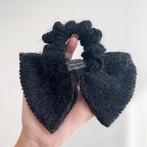 Detailopname van een zwarte gebreide strik haarelastiek met 'Hand Made' label.