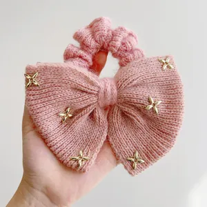 Detailopname van een roze gebreide strik-scrunchie met gouden sterren en woltextuur