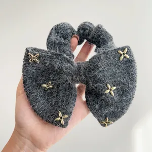 Gedetailleerde weergave van een pluizige grijze strik scrunchie met gouden sterhangers