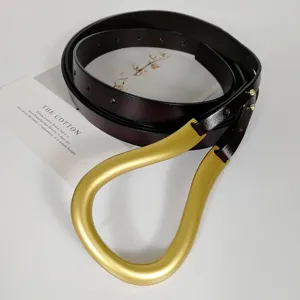 Close-up of women's dark brown genuine leather belt featuring a unique large gold horseshoe buckle.