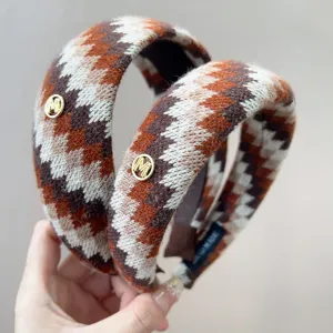 Detail van Fair Isle gebreide hoofdband met gouden M-embleem en zachte wollen textuur