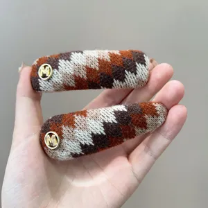 Detailweergave van gebreide haarclips met Fair Isle-patroon en gouden M-bedeltjes