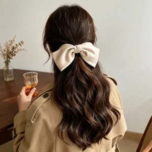 Close-up of an elegant cream satin 3D bow hair clip with a gold heart charm on wavy hair