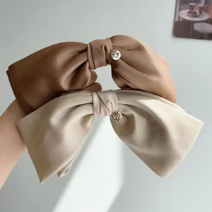 Close-up detail of elegant satin bow hair clips with gold heart charms in beige and brown