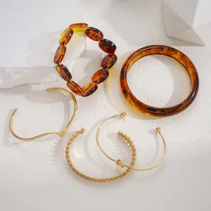 Dettaglio ravvicinato di bracciali rigidi in metallo dorato e resina color ambra
