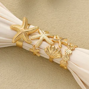 Detaillierte Ansicht goldener Seestern- und Muschelringe auf elegantem cremefarbenem Stoff