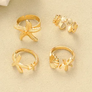 Detailansicht von 4 goldenen Ringen mit Seestern- und Muschelmotiven auf Sand.