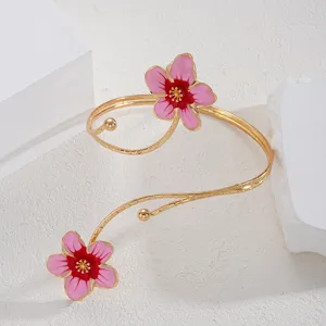 Dettaglio di eleganti fiori in smalto rosa su un bracciale da braccio regolabile dorato.
