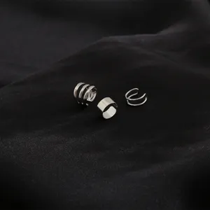 Close-up of minimalist silver multi-layer ear cuffs on black satin fabric.