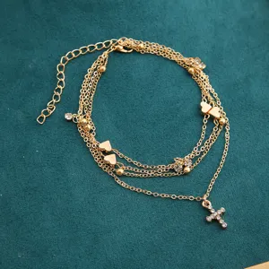 Close-up detail of a layered gold anklet with heart charms and a sparkling cross pendant.