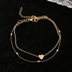 Close-up of a double-layer gold anklet featuring a heart charm and elegant bead accents