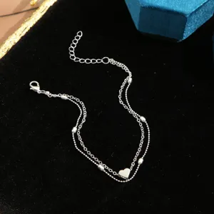 Macro view of double-layer silver tone anklet featuring a polished heart charm and beads