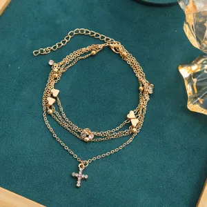 Close-up of elegant multi-layered gold anklet featuring heart and rhinestone cross charms.