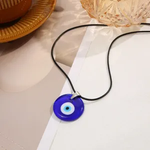Macro detail view of a vibrant blue glass Evil Eye pendant with a black cord necklace.