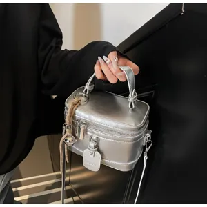Detail view of the silver metallic box bag with a top handle and tassel charm.