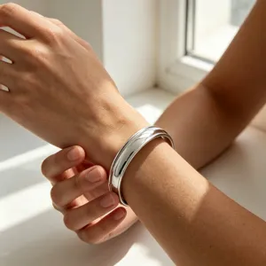 Gros plan détail du large bracelet rigide en acier inoxydable à double fente au poignet, brillant.