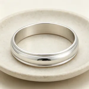Gros plan detail d'un large bracelet jonc en acier inoxydable a double rainure dans une assiette.