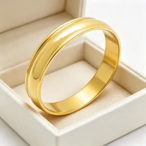 Gros plan sur les détails du large bracelet jonc en acier doré dans la boîte bijou.