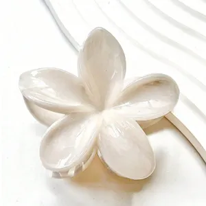 Gros plan sur une pince à cheveux fleur de frangipanier avec effet nacre marbré blanc