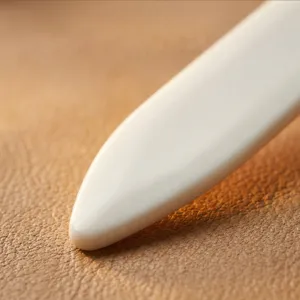 Primo piano di piegacarte in plastica e strumento per pelle, finitura avorio liscia e pulita.