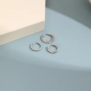 Detail view of three silver-colored C-shaped ear cuffs with rhinestone and textured designs.