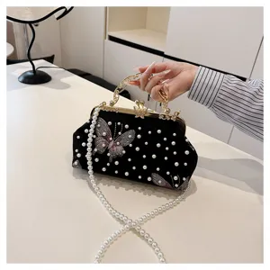 Detalle de bolso de mano de terciopelo negro con bordado de mariposa y cadena de perlas