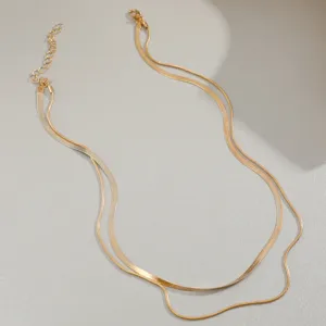 Detail view of a golden double-layered necklace featuring a flat snake bone chain.