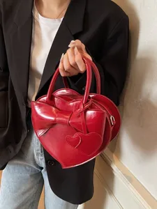 Elegante bolso de mano rojo con forma de corazón y lazo grande llevado por una modelo