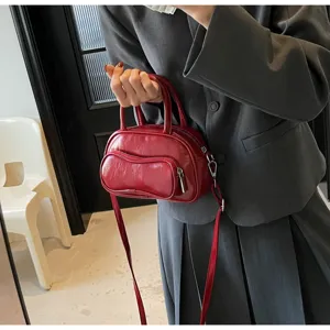 Detail shot of a trendy red soft leather bowling bag held by a model in a grey suit.